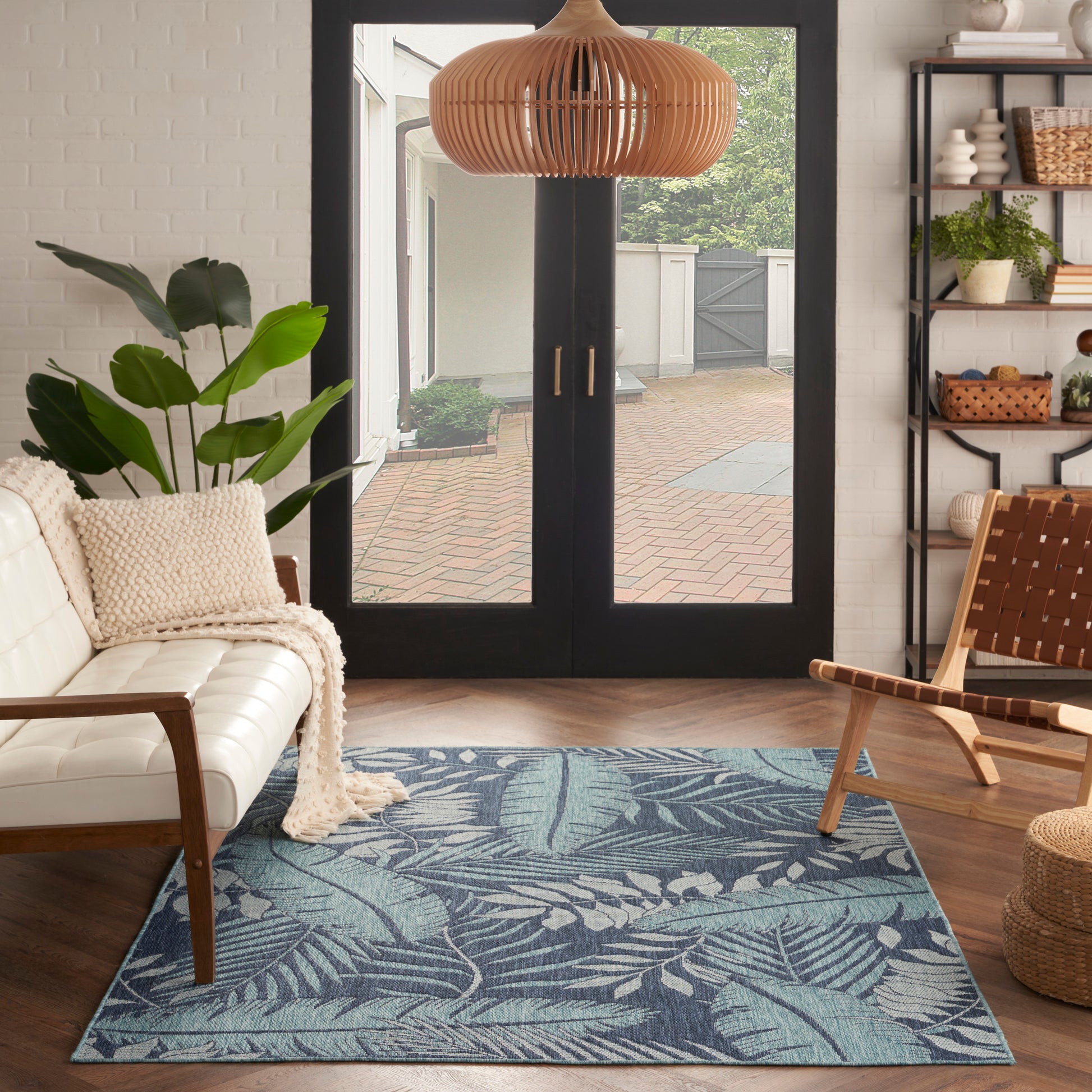 Rectangular blue palm-leaf patterned area rug in a modern living room with white sofa and wooden chair.