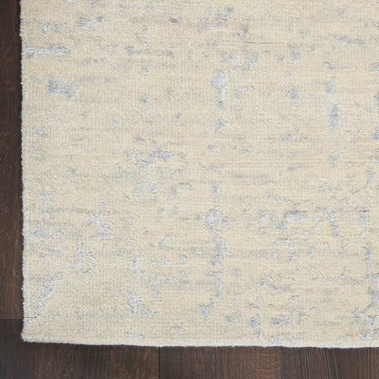 Cream beige rectangular rug with subtle blue-gray abstract pattern and soft plush pile on dark wooden floor.