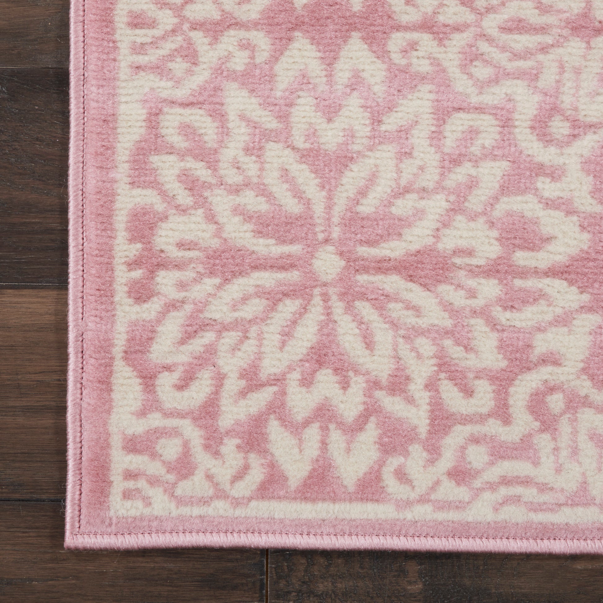Pink & white runner rug with a central floral damask pattern and pink border on a wooden floor.