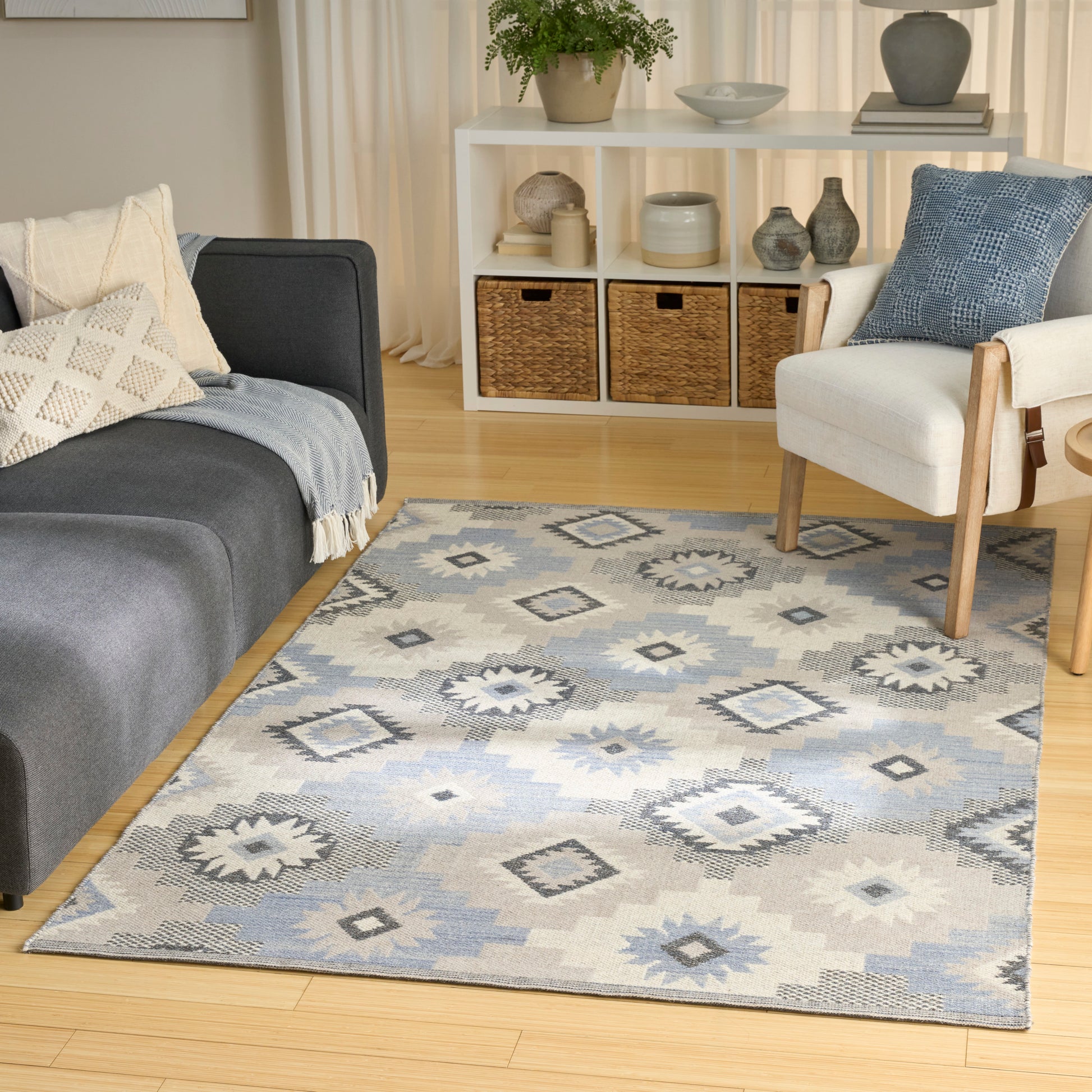 Geometric diamond-patterned area rug in light blue, gray and beige on a wooden floor, in a modern living room with gray sofa and white armchair.