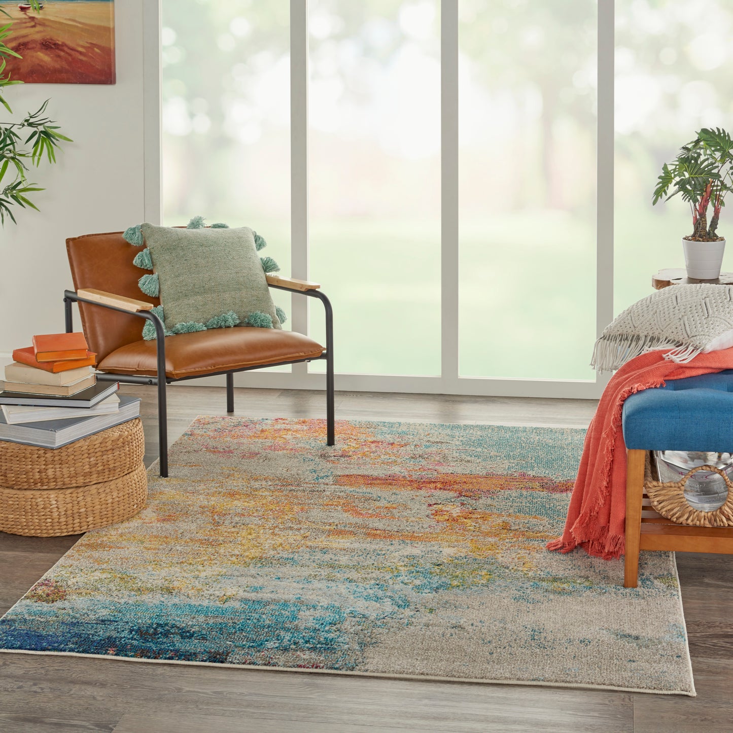 Boho living room rug with abstract multicolor pattern; tan leather chair, teal fringe pillow, woven ottoman, blue bench.
