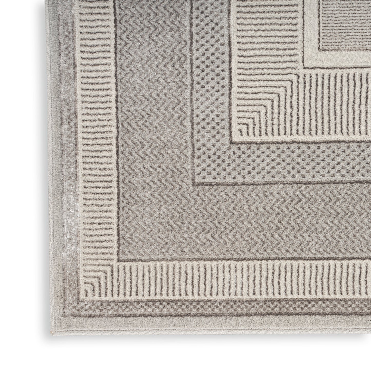 Beige textured rug with layered rectangular borders and chevron, dot and line patterns.