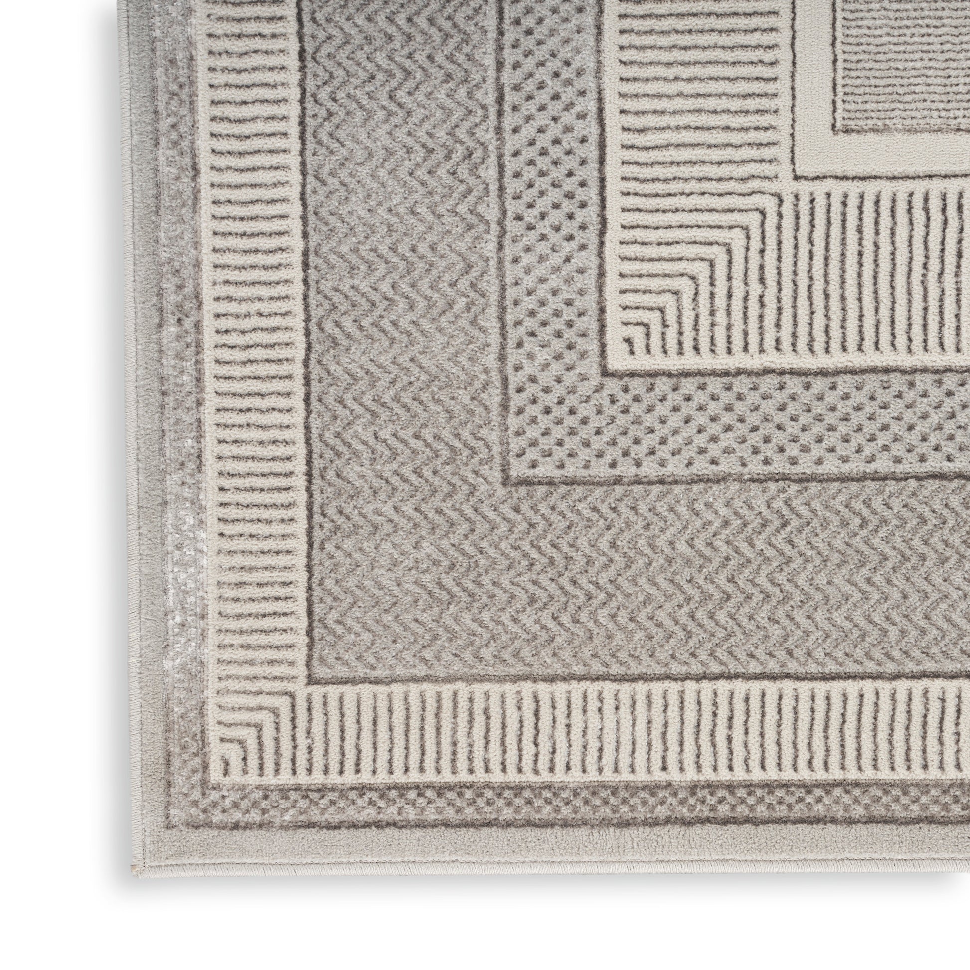 Beige textured rug with layered rectangular borders and chevron, dot and line patterns.