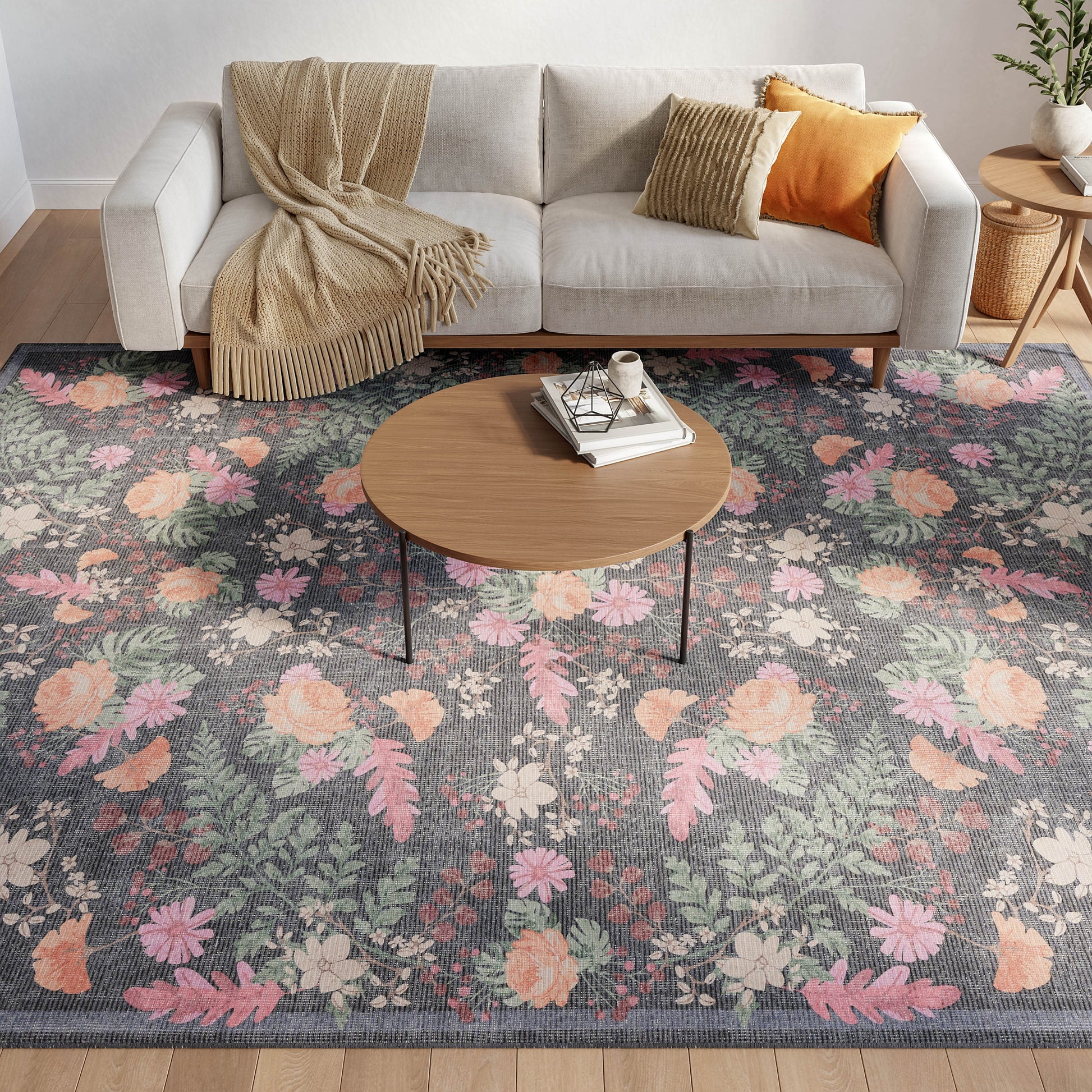 Gray floral area rug with pink, peach and green blossoms beneath a round wood coffee table beside a beige sofa.