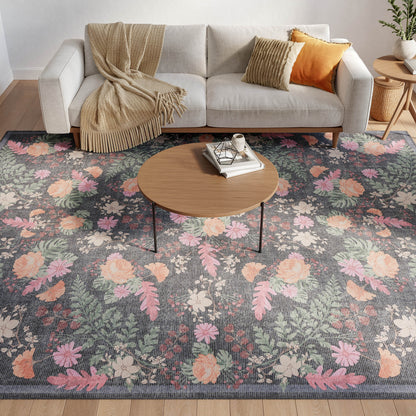 Gray floral area rug with pink, peach and green blossoms beneath a round wood coffee table beside a beige sofa.