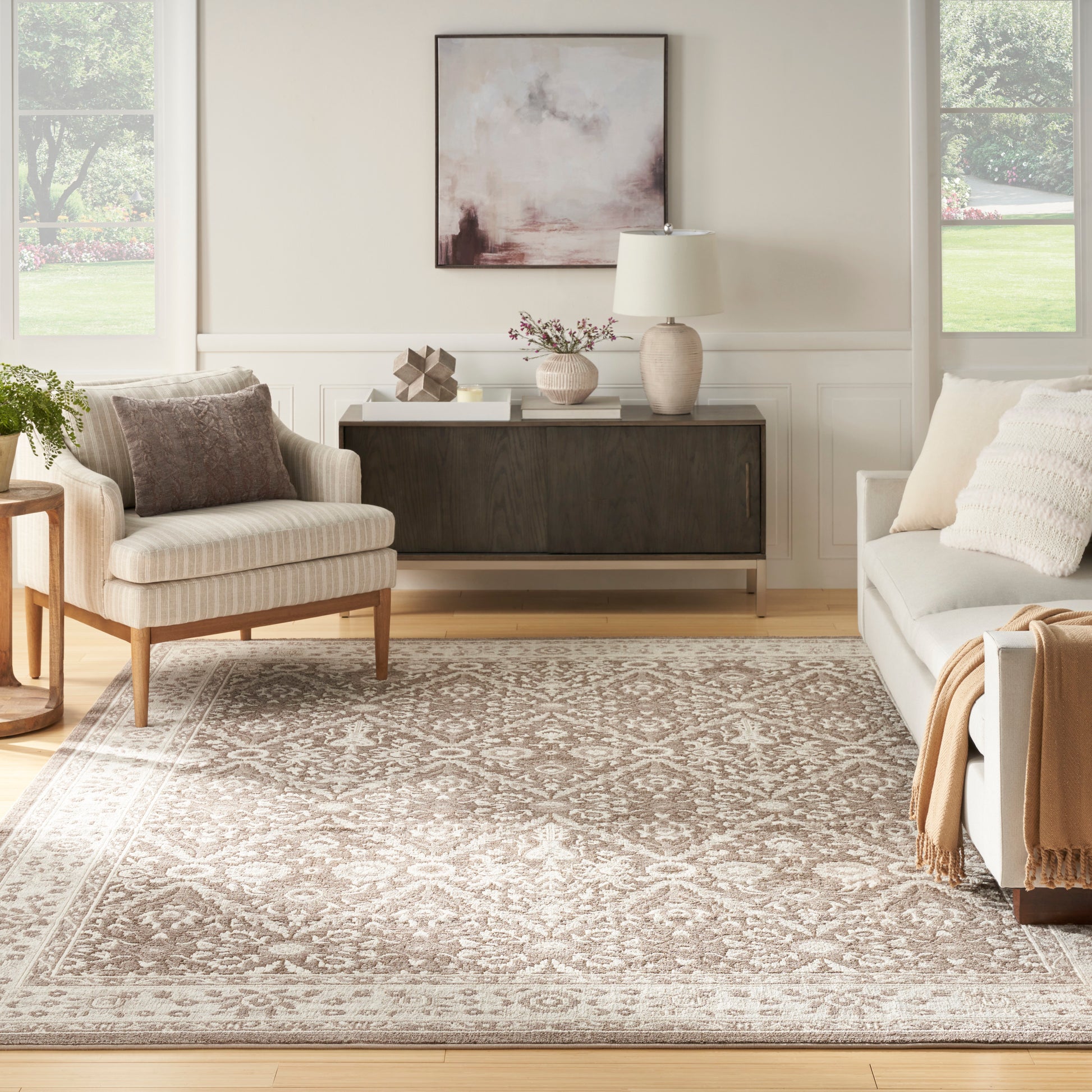Neutral living room with beige armchair, gray sofa, patterned beige rug, dark wood sideboard, and soft abstract art.