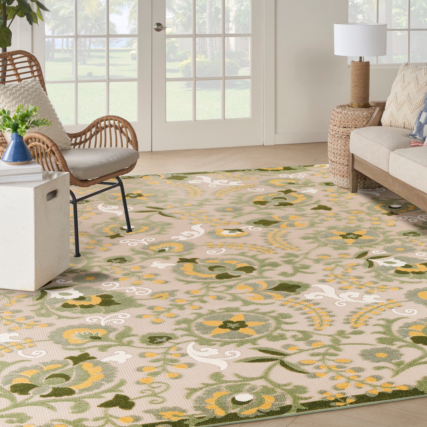 Living room with beige floral area rug in greens and yellows, wicker chairs, beige sofa, and woven lamp.