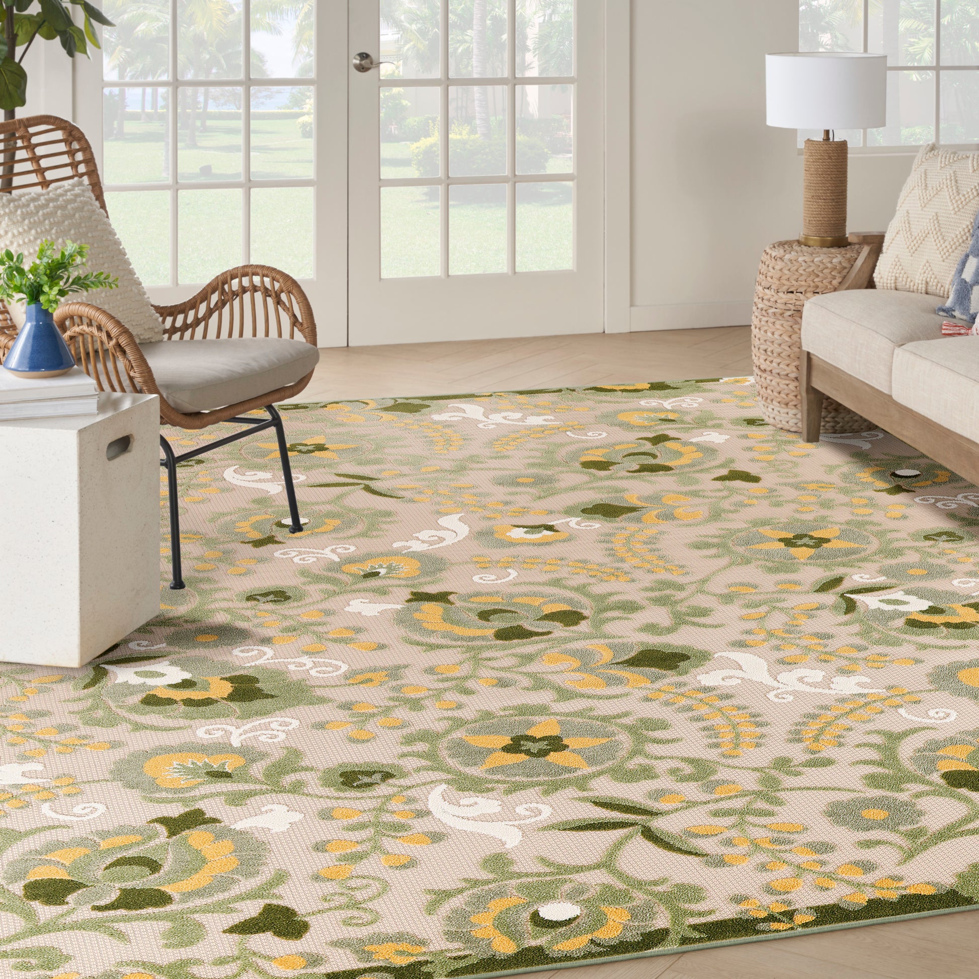 Living room with beige floral area rug in greens and yellows, wicker chairs, beige sofa, and woven lamp.