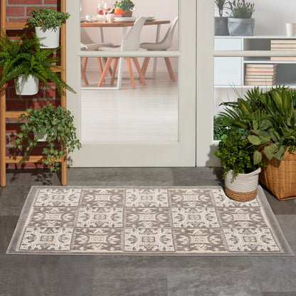 Rectangular patterned rug with cream and gray tile motifs at a glass-door entry, flanked by potted plants.