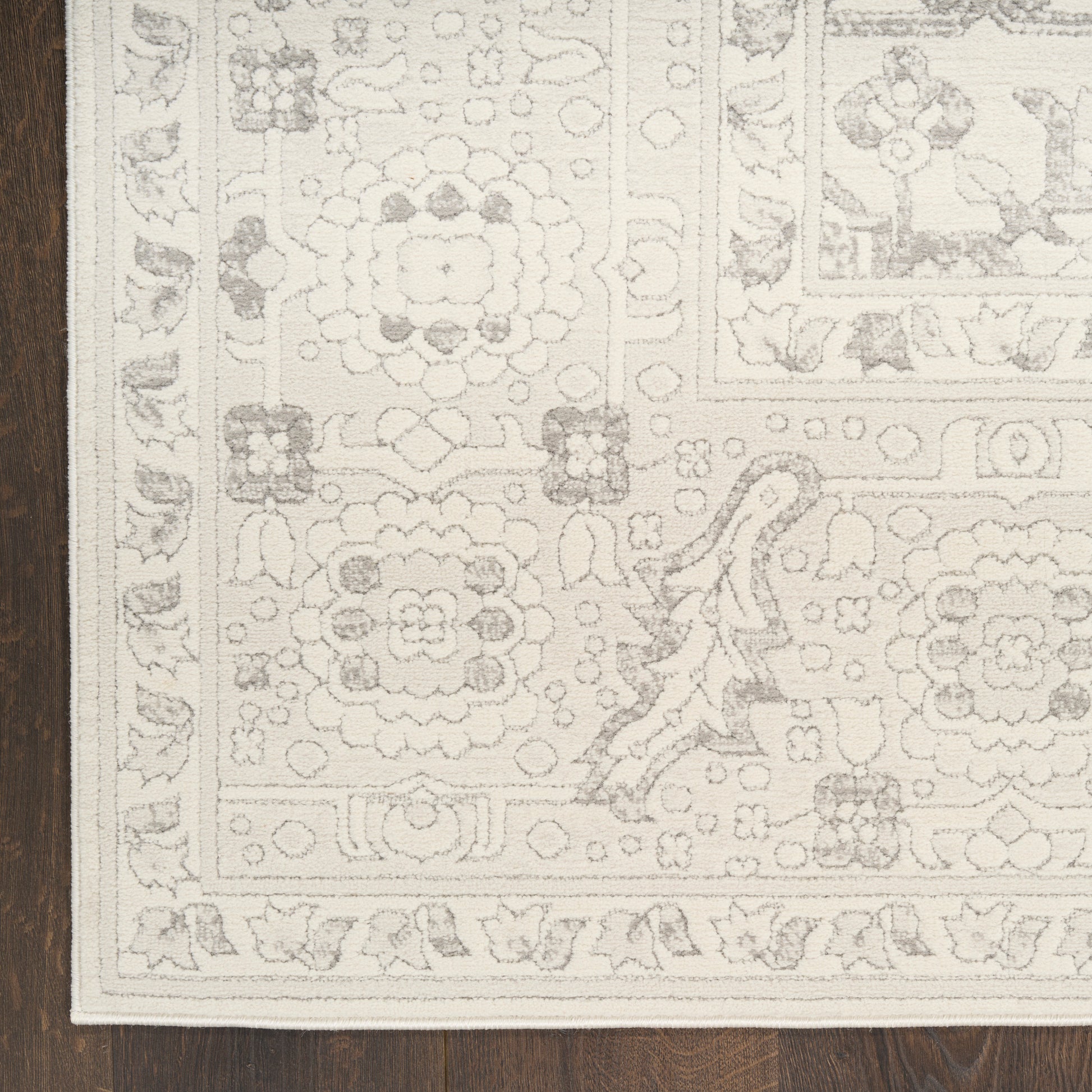 Cream area rug with ornate floral medallions and border on dark wood floor.