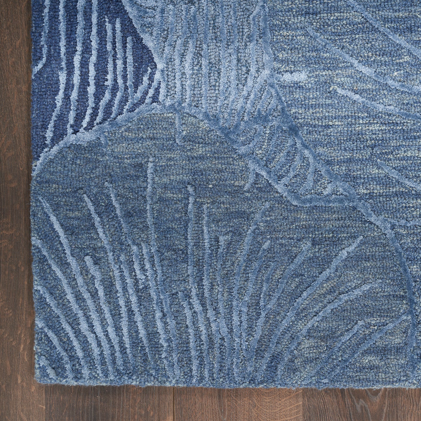 Blue abstract-pattern area rug with palm-leaf motifs and varying blue tones on a wooden floor.