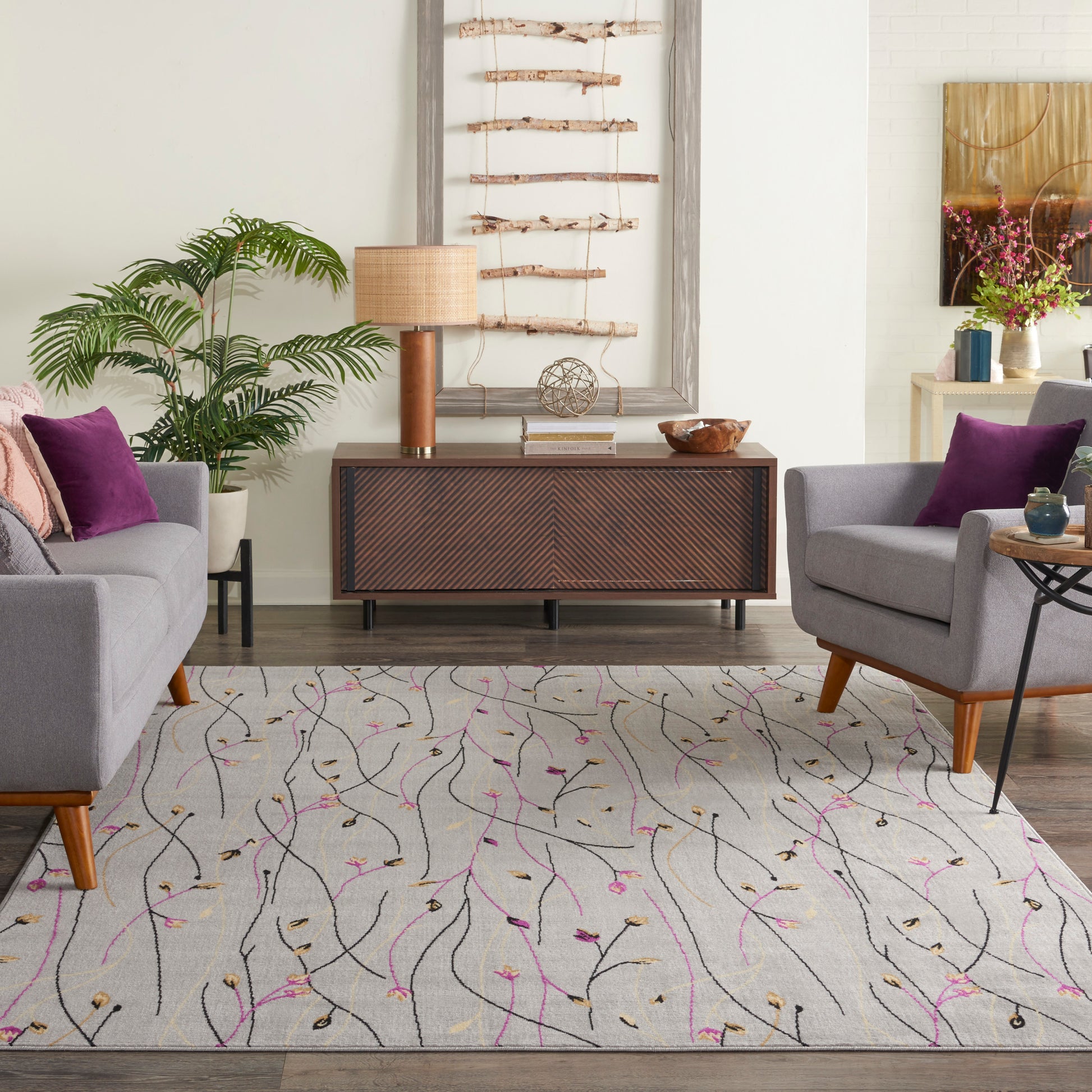 Living room with a light gray patterned rug, mid-century wood console, two gray armchairs with purple cushions.