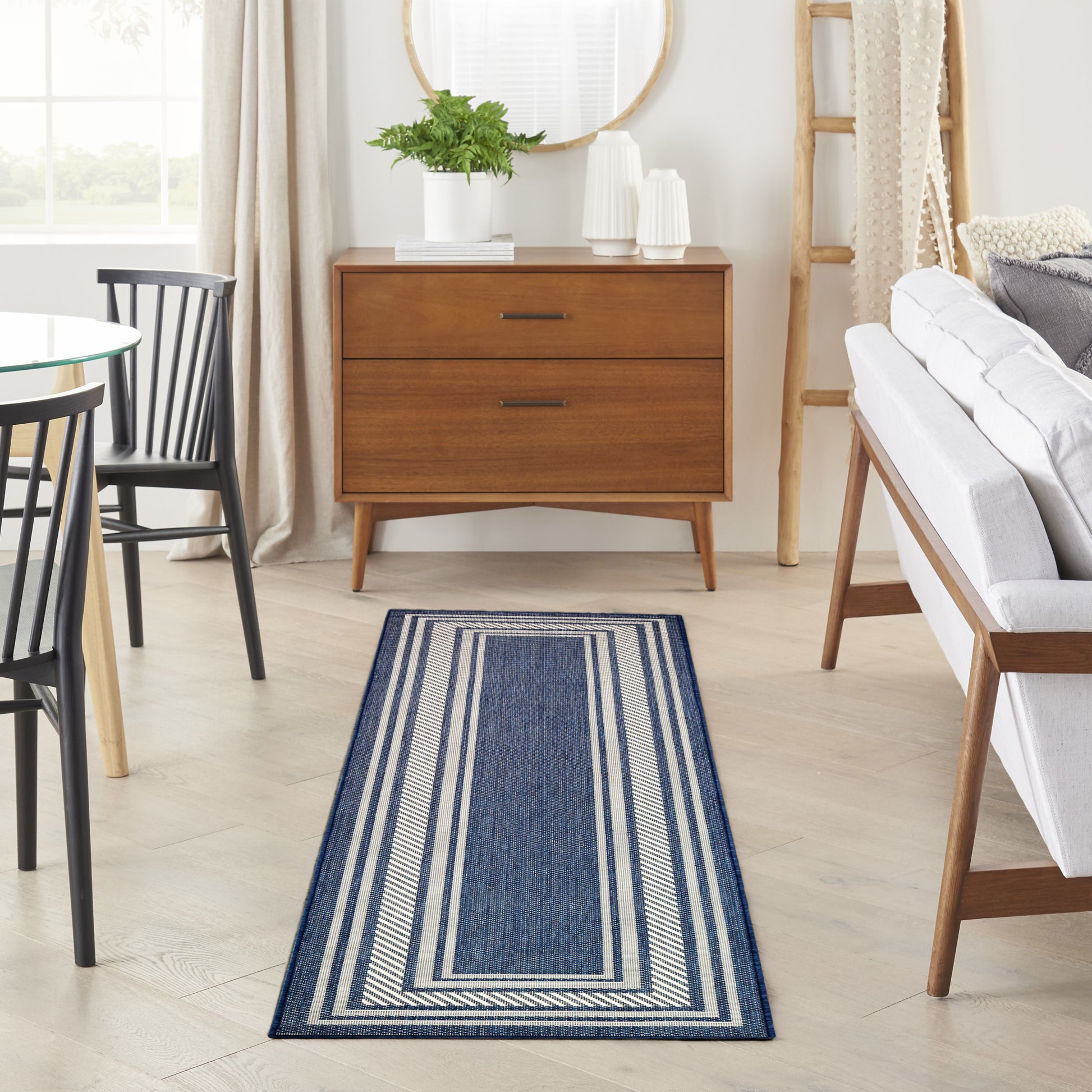 Blue striped runner rug in a bright mid-century living room with a wooden dresser, round glass table, and a white sofa.