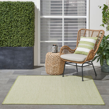 Outdoor rug in light green, 4' x 4' square, under wicker seating with cream cushions and a green striped pillow beside a woven round side table.