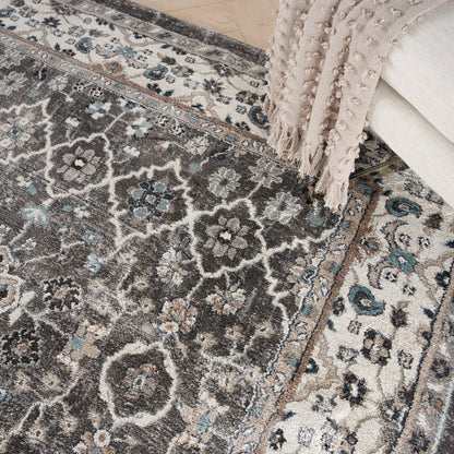 Ornate gray-blue area rug with ivory floral medallions and borders; beige tassel throw draped over edge.