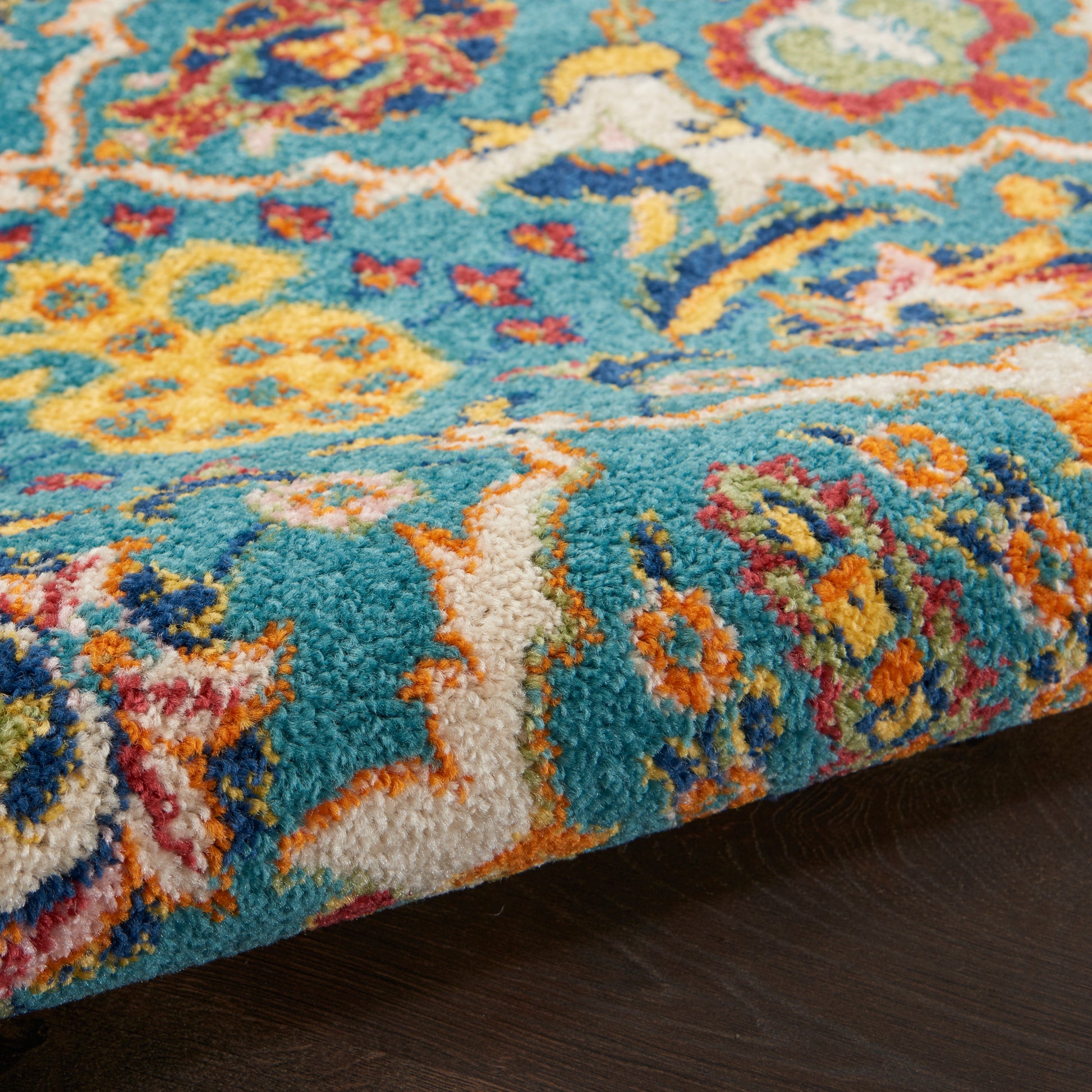 Vibrant turquoise oriental rug with multicolor floral pattern; thick plush pile, folded edge on dark wood floor.