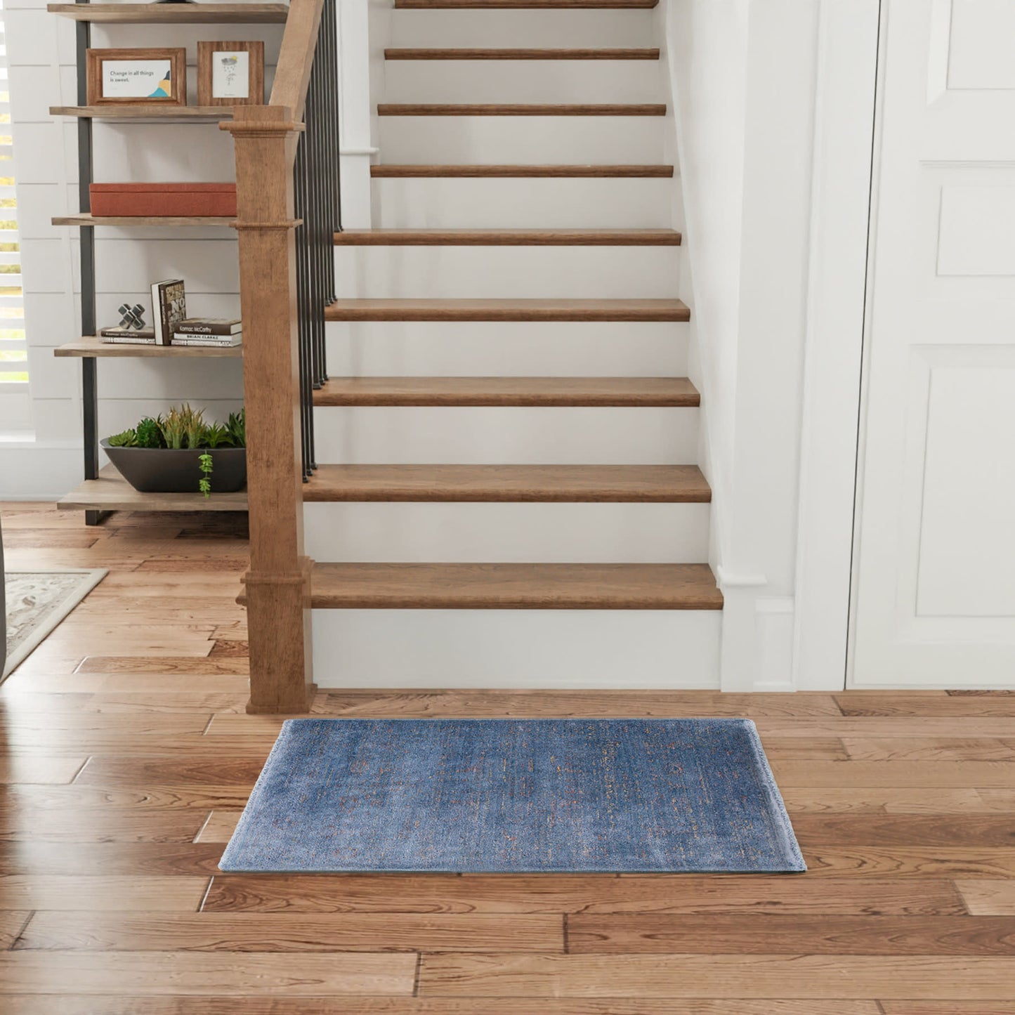 Blue rectangular rug on warm wood floor beside a wooden staircase with black metal balusters in a bright entryway.