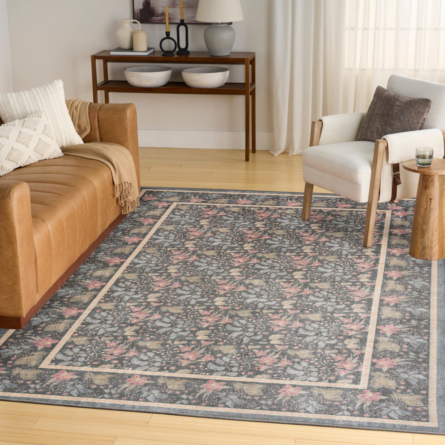 Blue floral area rug with a pale border in a bright living room, paired with a tan leather sofa and beige armchair.