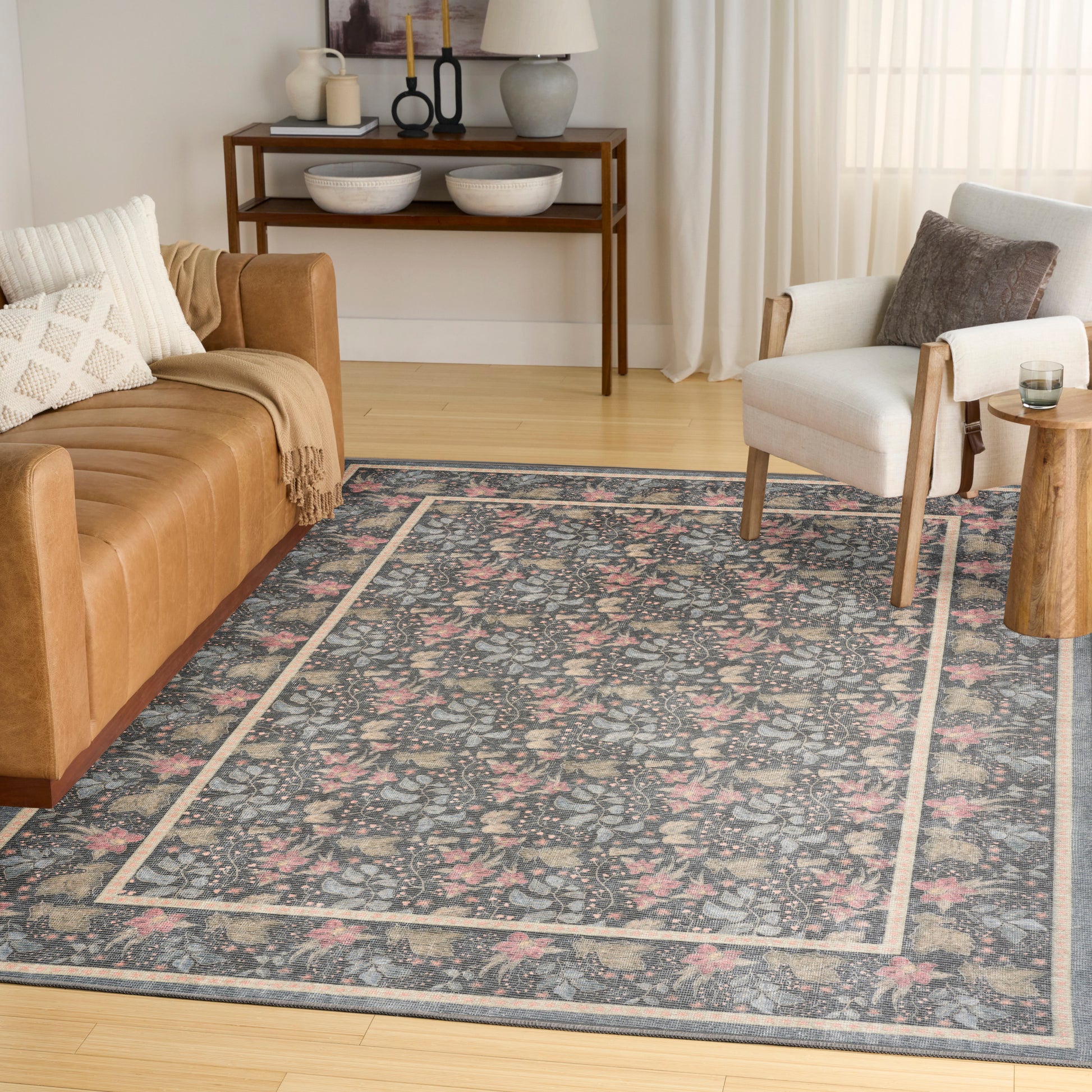 Blue floral area rug with a pale border in a bright living room, paired with a tan leather sofa and beige armchair.