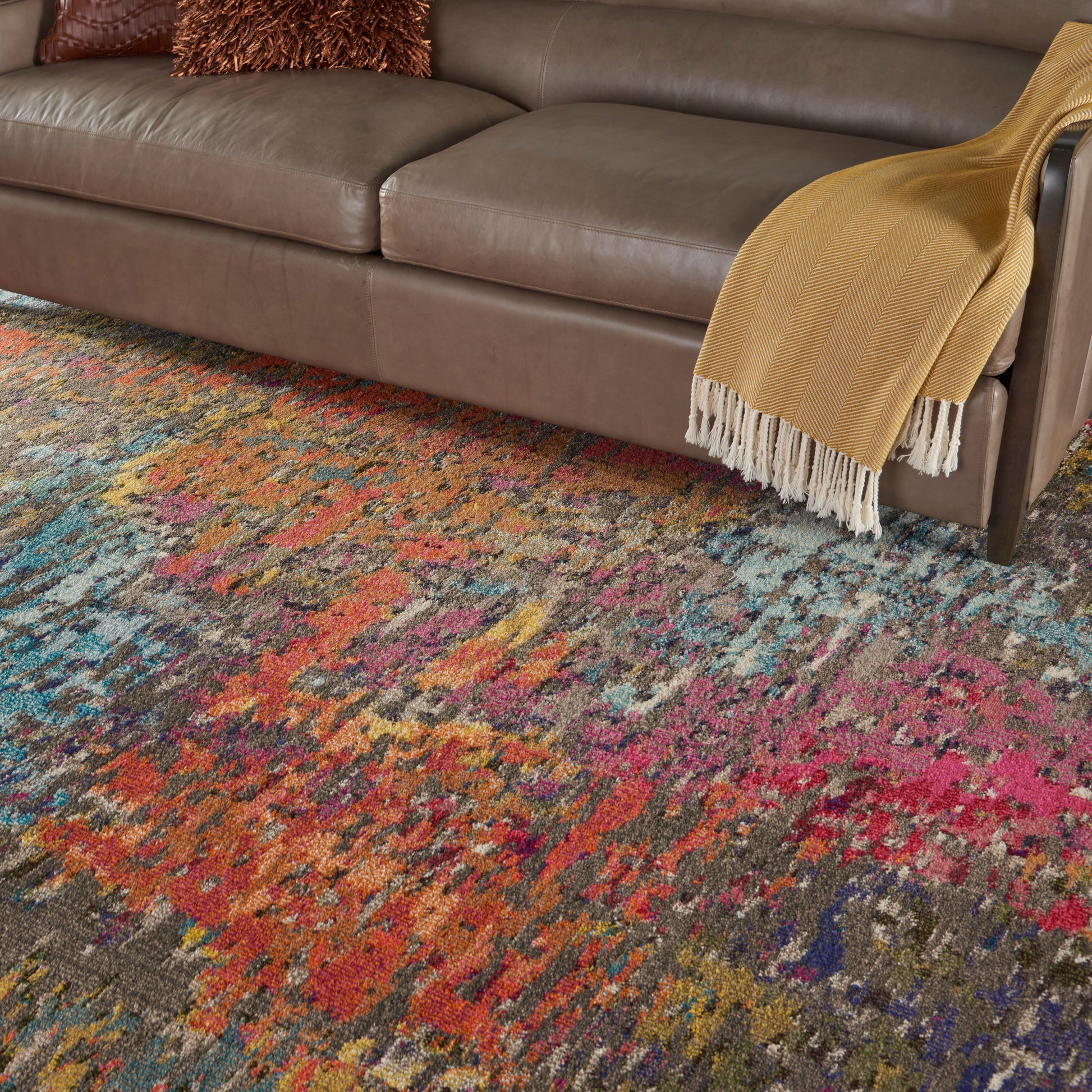 Brown leather sofa with mustard-yellow throw blanket draped over arm; multicolor abstract rug beneath.