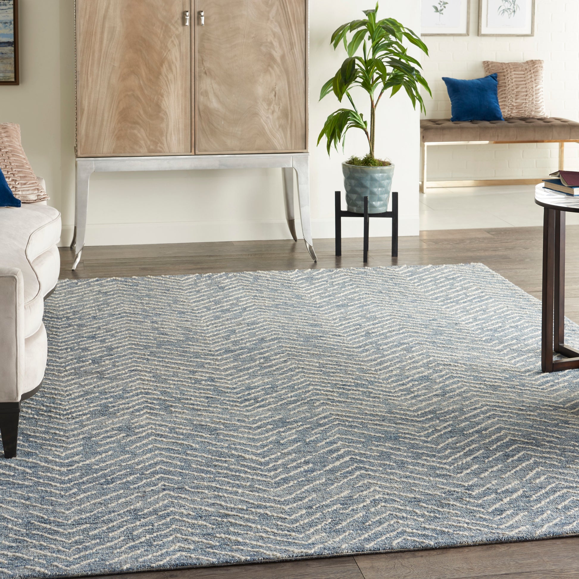 Blue-gray zigzag patterned area rug anchors a cozy living room with beige sofa, light wood cabinet, and potted plant.