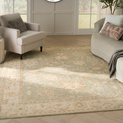 Living room with a large ornate area rug in ivory, sage and tan tones; two light gray chairs and a curved sofa; neutral decor.