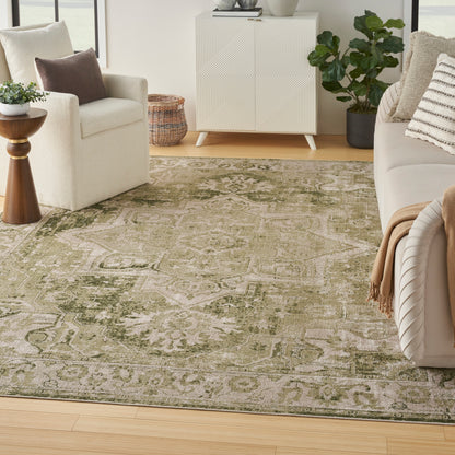 Olive green and beige patterned area rug in a bright living room with a cream sofa, white geometric cabinet, and plants.