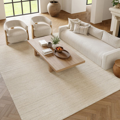 Neutral living room with beige fabric sofa, two cream armchairs, a light wooden coffee table on a cream rug.