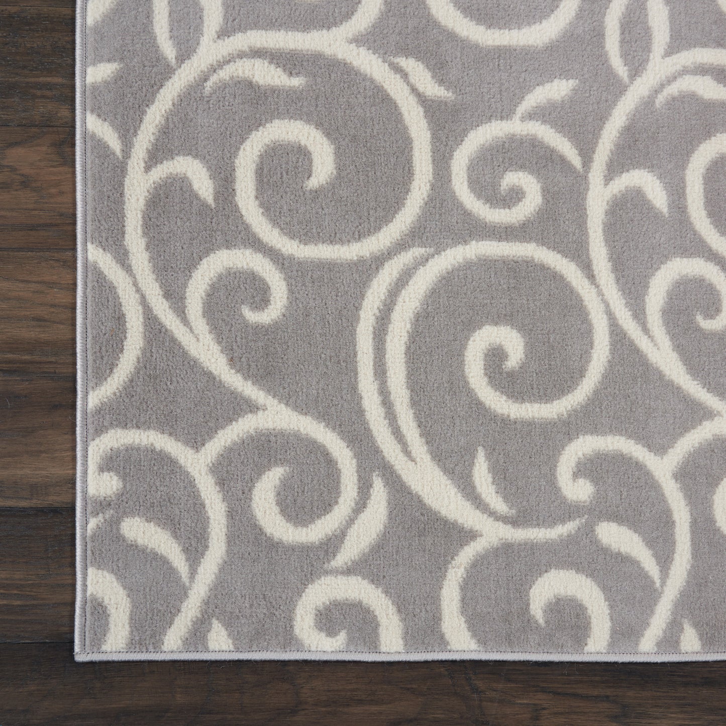 Grey rug with ivory scroll pattern, soft plush pile and visible stitched edge.