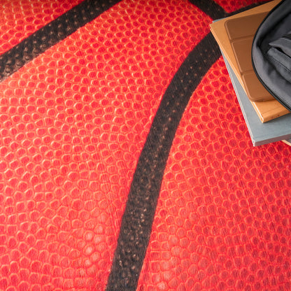 Close-up of red basketball texture with black seam; corner shows a gray zip pouch and orange notebooks.