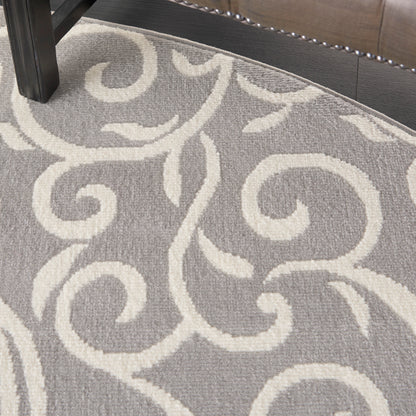 Gray round area rug with ivory scrolling vine motif; plush pile, under a dark wood furniture leg.