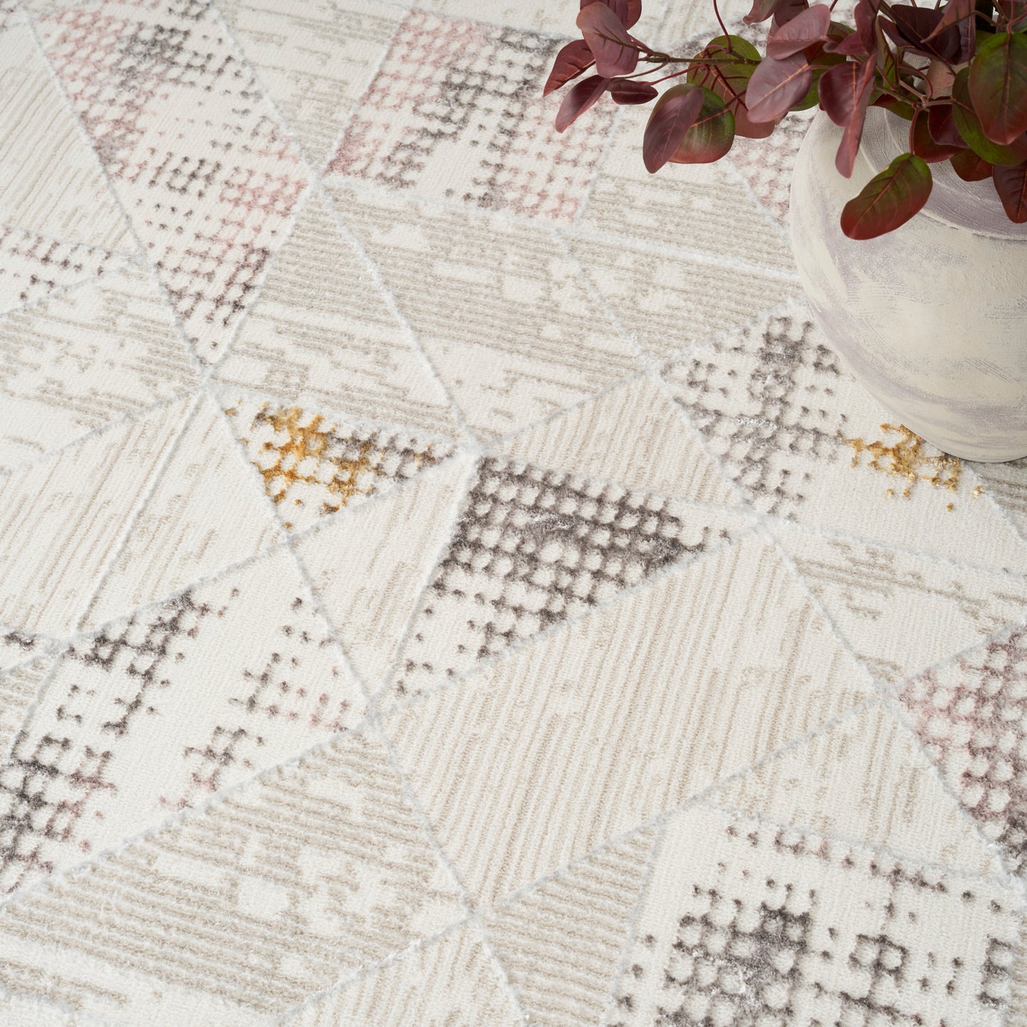 Neutral patchwork rug with geometric triangles in creams and beiges; ribbed texture, corner plant in a glass vase.