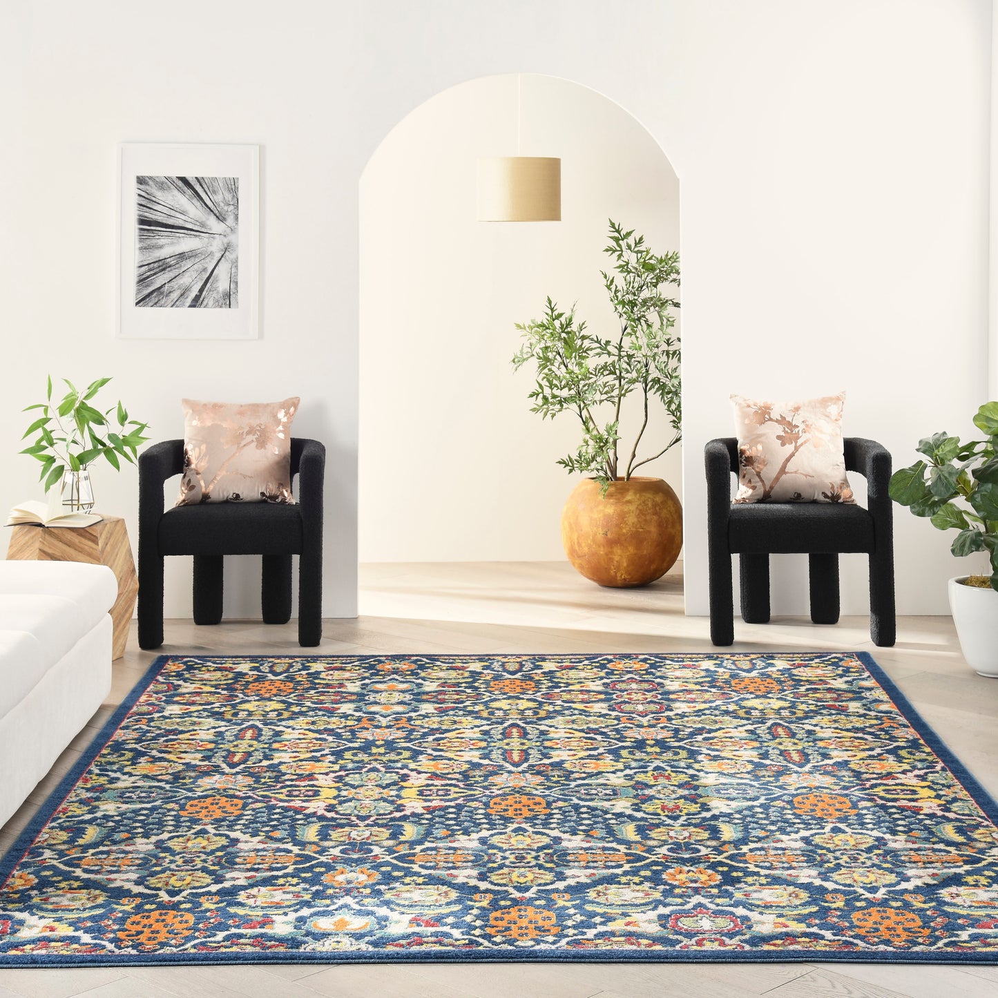 Rectangular oriental-inspired rug in blues, oranges and creams in a bright living room with two black chairs and plants.