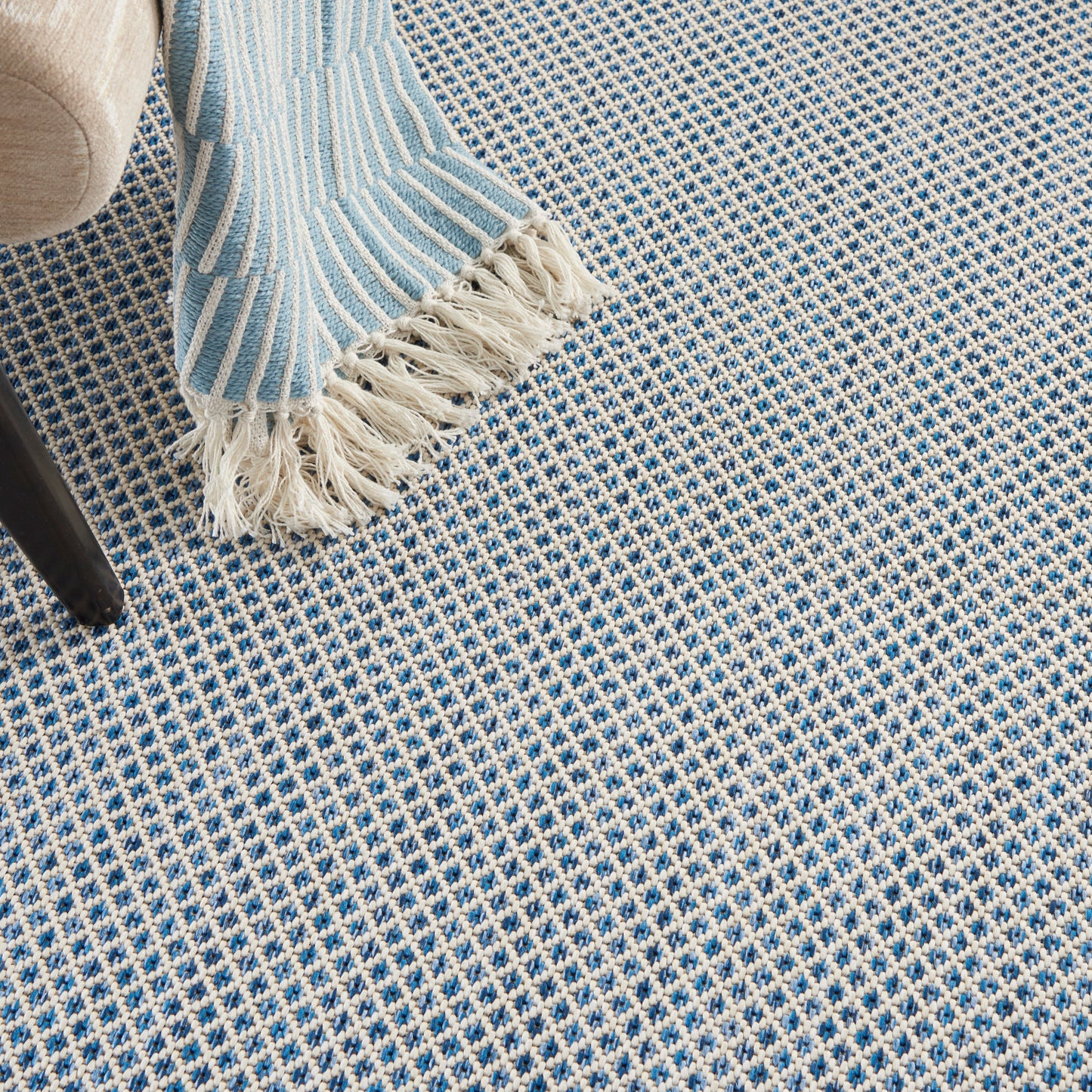 Blue and white woven checkered rug with fringe edging; light-blue striped throw draped over a chair leg.