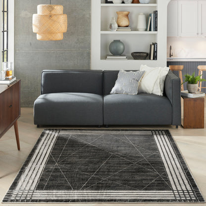 Dark gray modular sofa with white and gray cushions on a black geometric area rug in a modern living room.