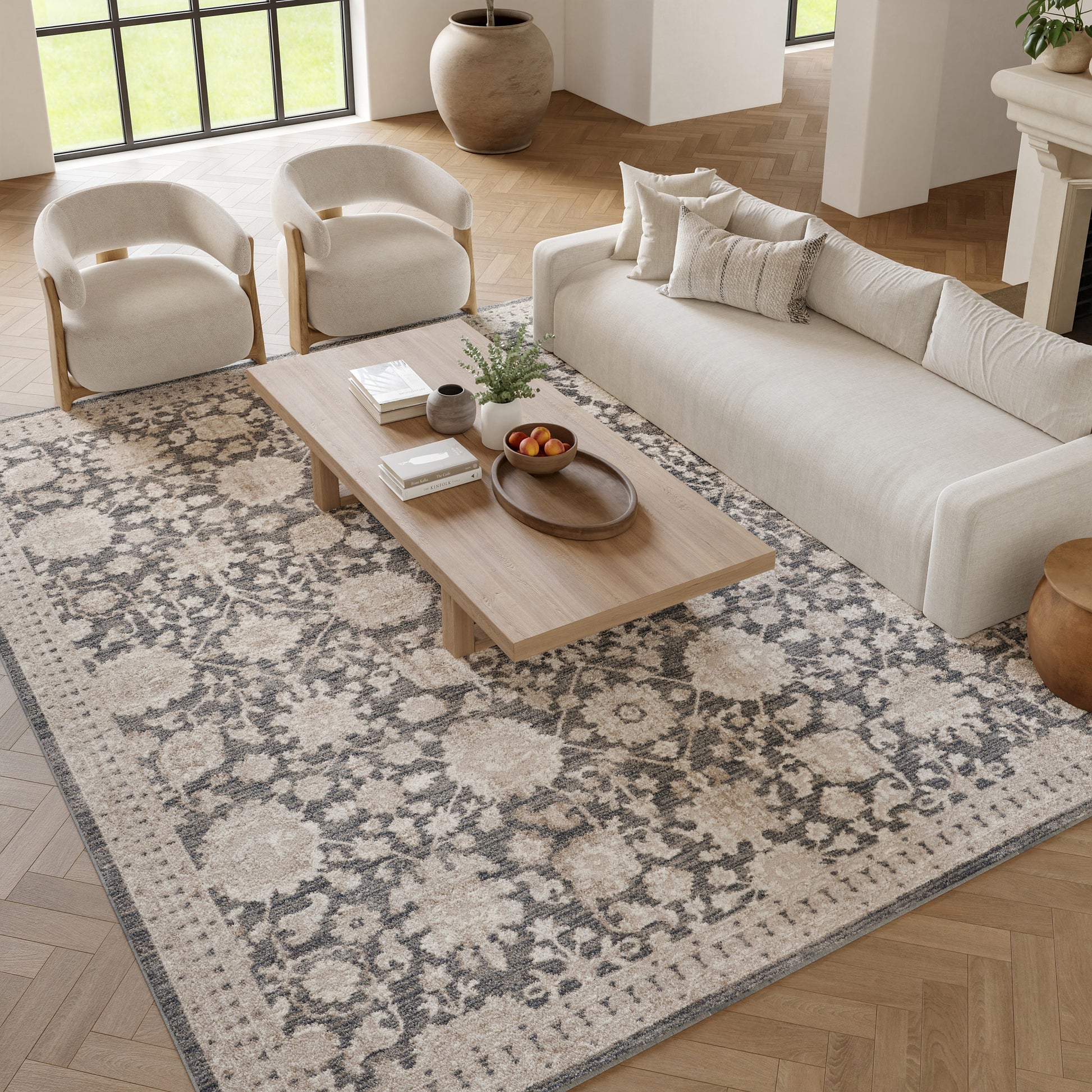 Neutral living room with beige sofa, two cream armchairs, a wooden coffee table, and a floral gray-beige rug.