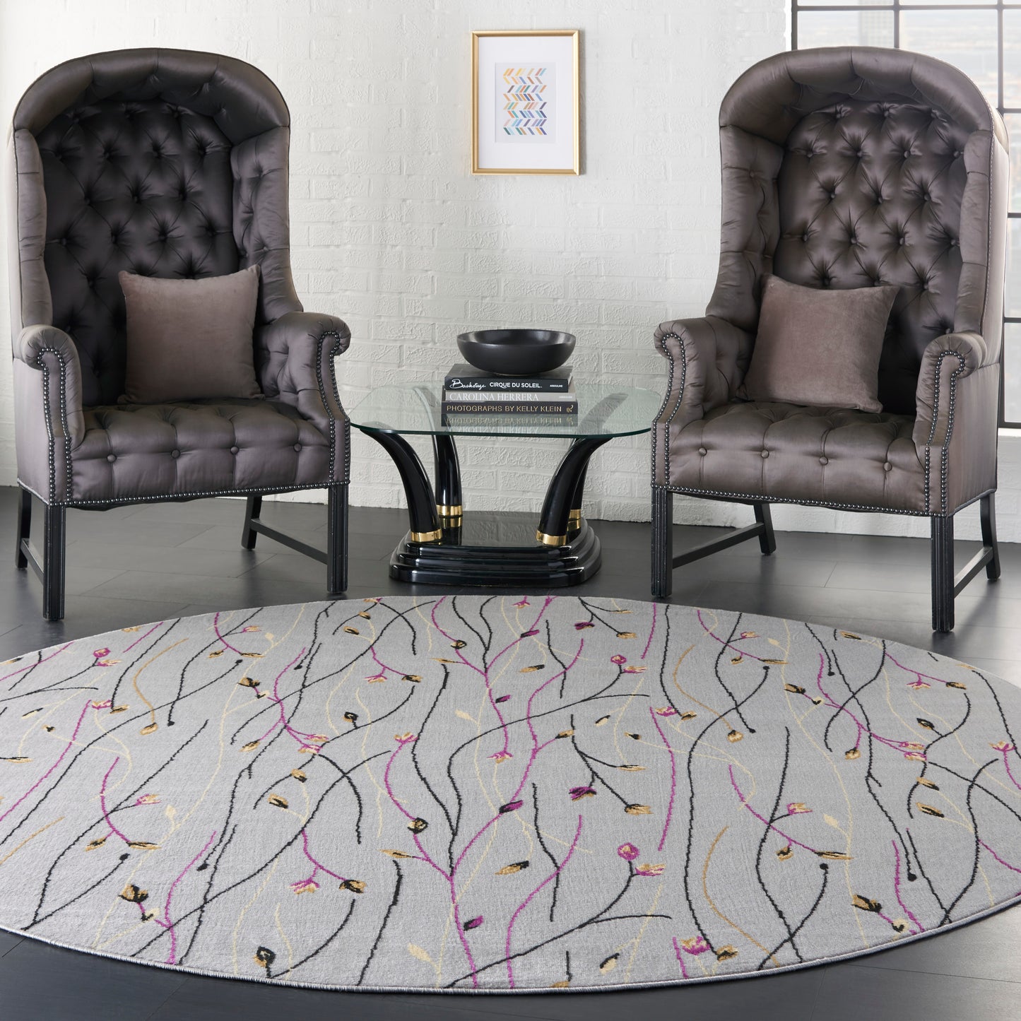 Round, light-patterned rug beneath two dark gray tufted leather club chairs with nailhead trim and a glass coffee table.