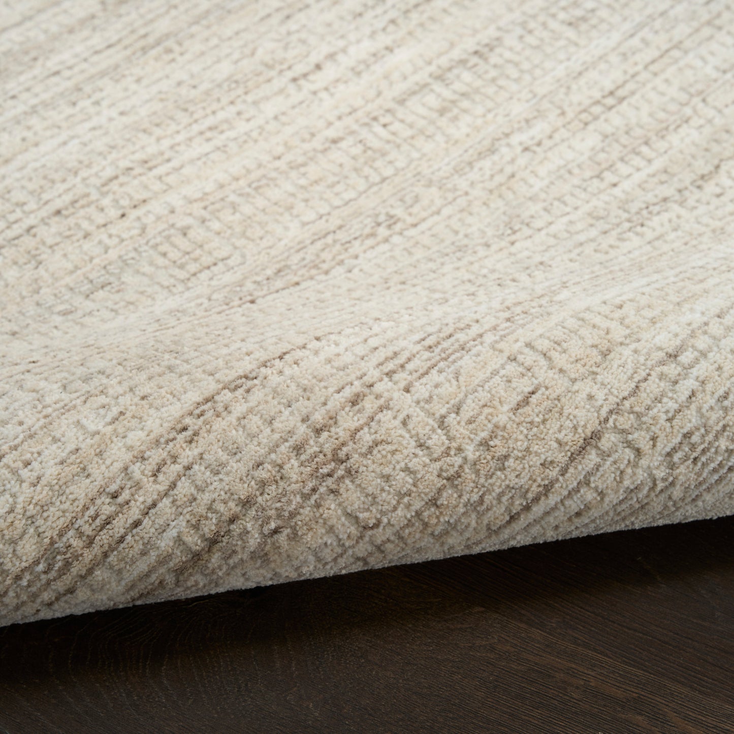 Beige, plush-area rug with textured pile and subtle pattern, folded edge on dark wood floor.