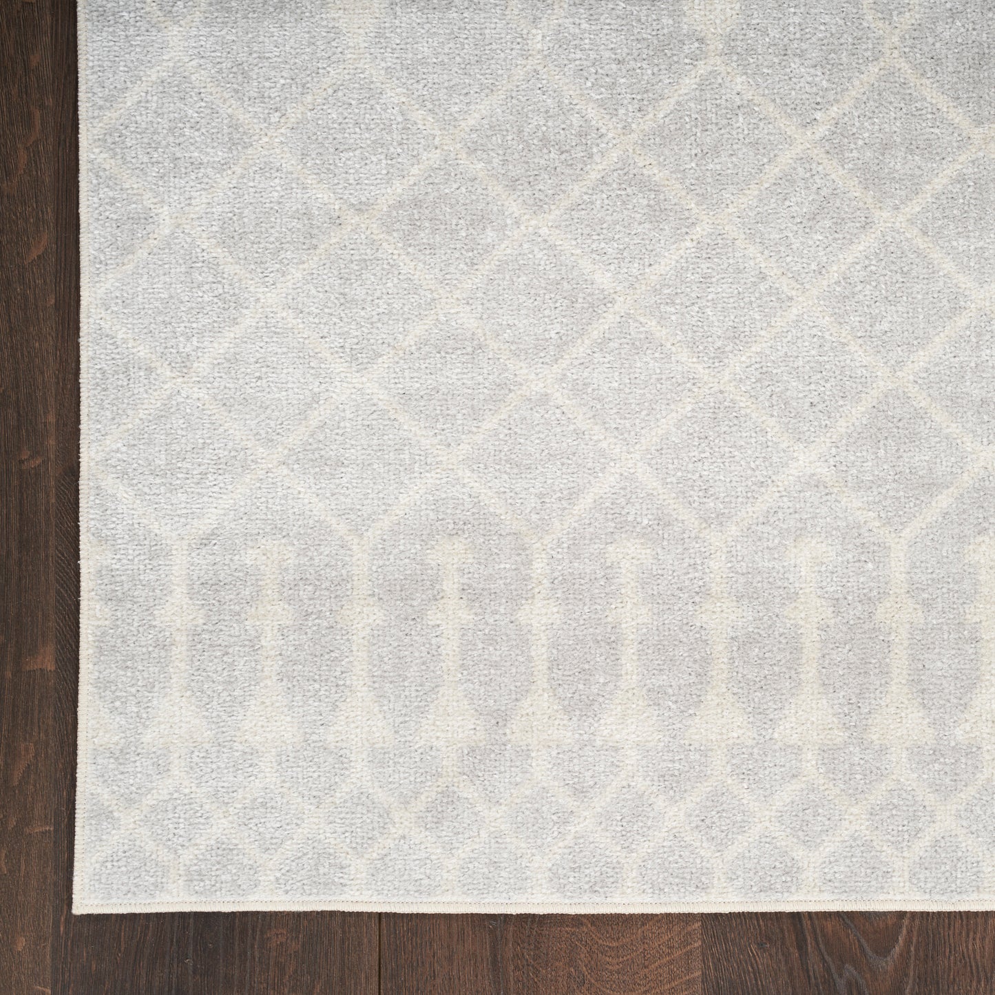 Light gray geometric area rug with trellis diamonds and arched border on dark wood floor.