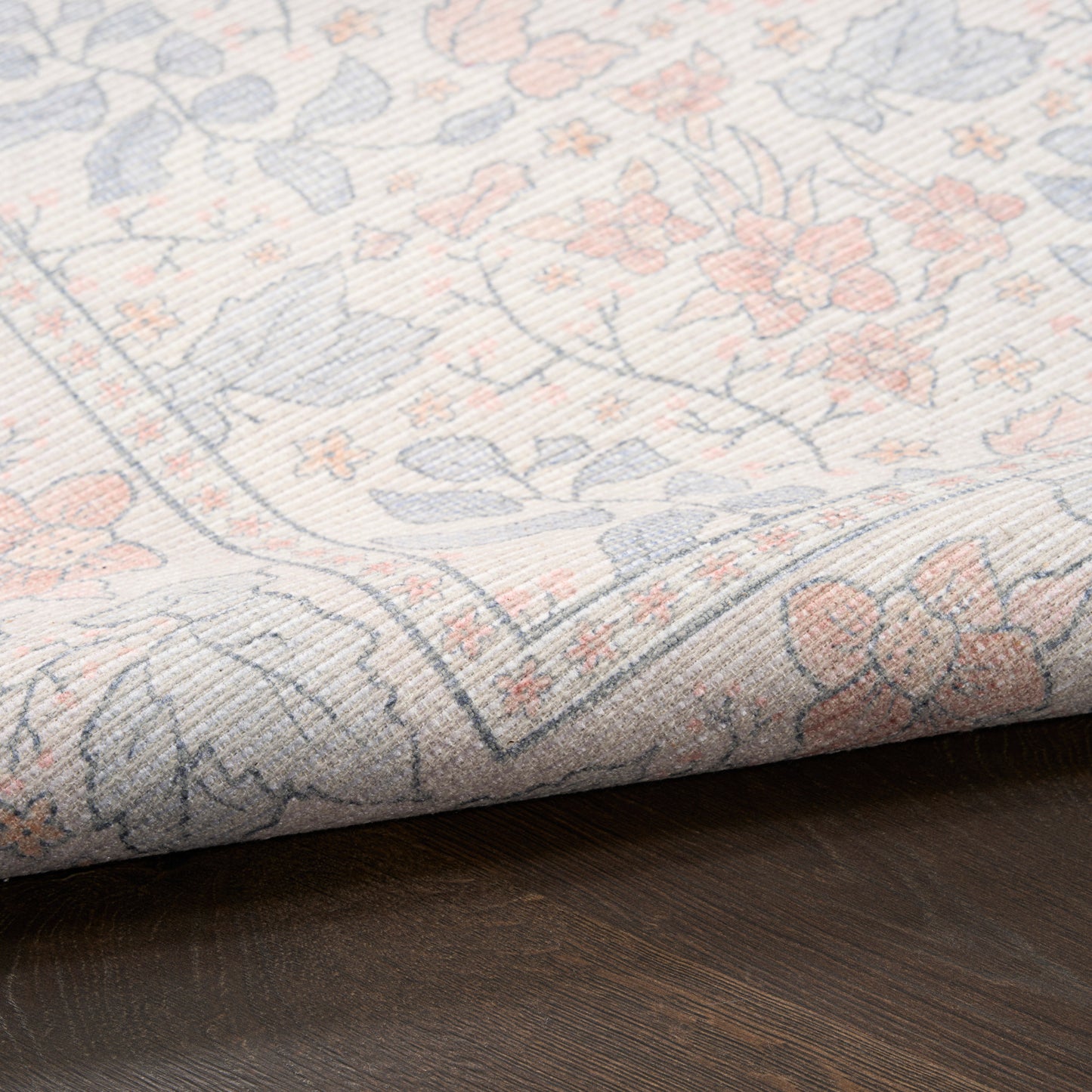 Pastel floral woven rug in pale blue, pink and beige, folded at the edge on dark wood floor.