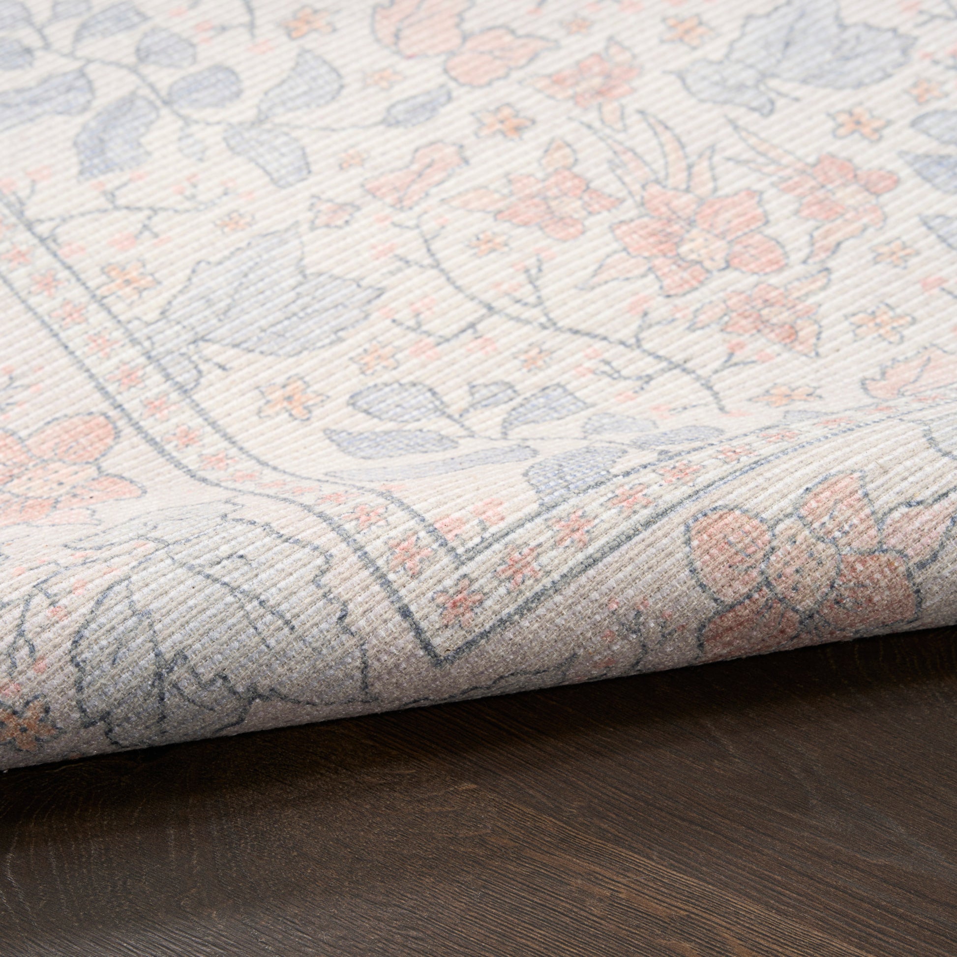 Pastel floral woven rug in pale blue, pink and beige, folded at the edge on dark wood floor.