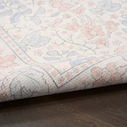 Pastel floral woven rug in pale blue, pink and beige, folded at the edge on dark wood floor.