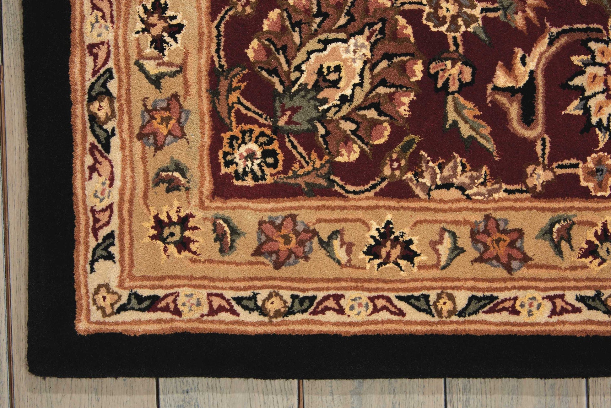 Persian-style area rug with burgundy center, ivory border and floral vines; wool texture on wooden floor.