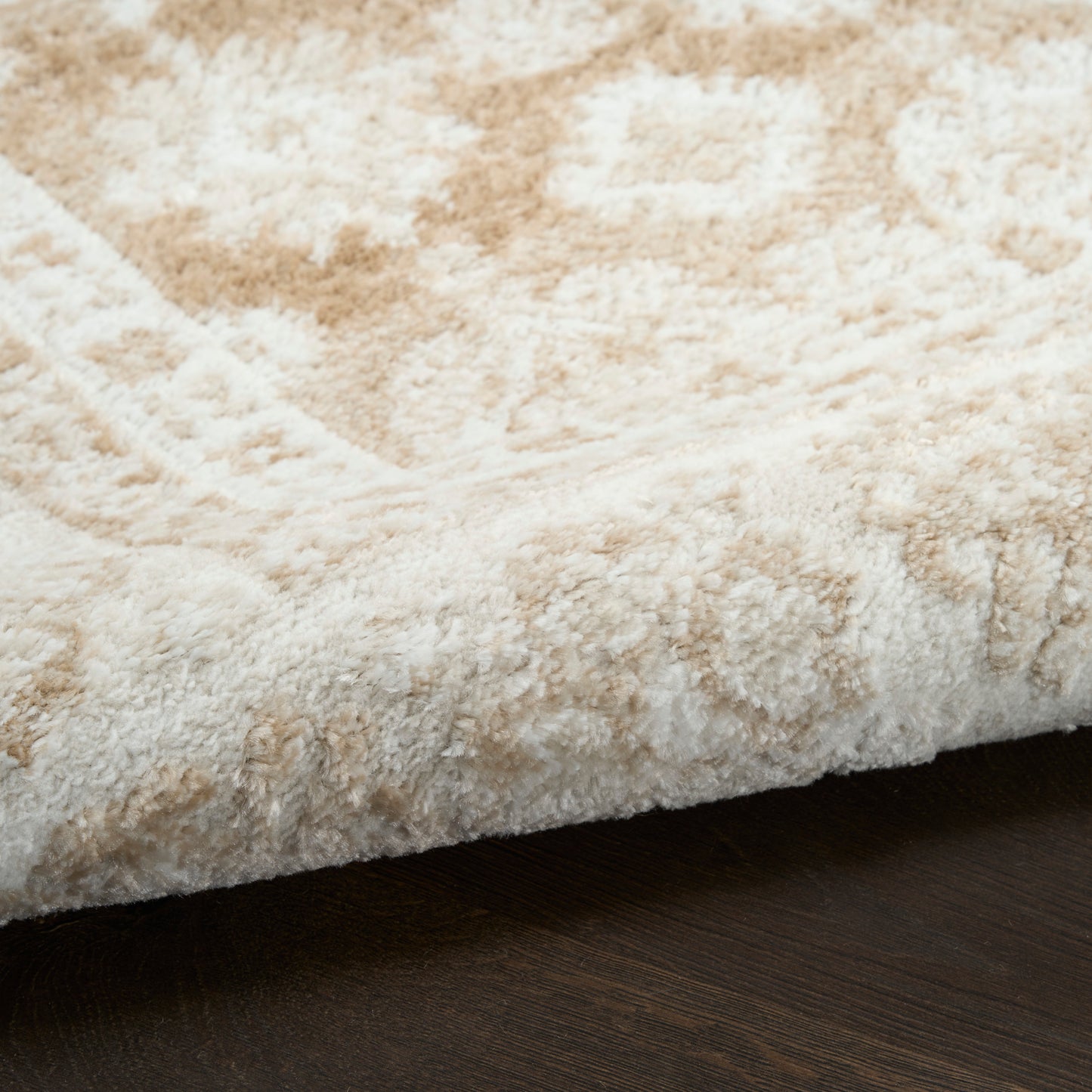 Close-up of a plush beige and cream shag rug edge resting on a dark wood floor