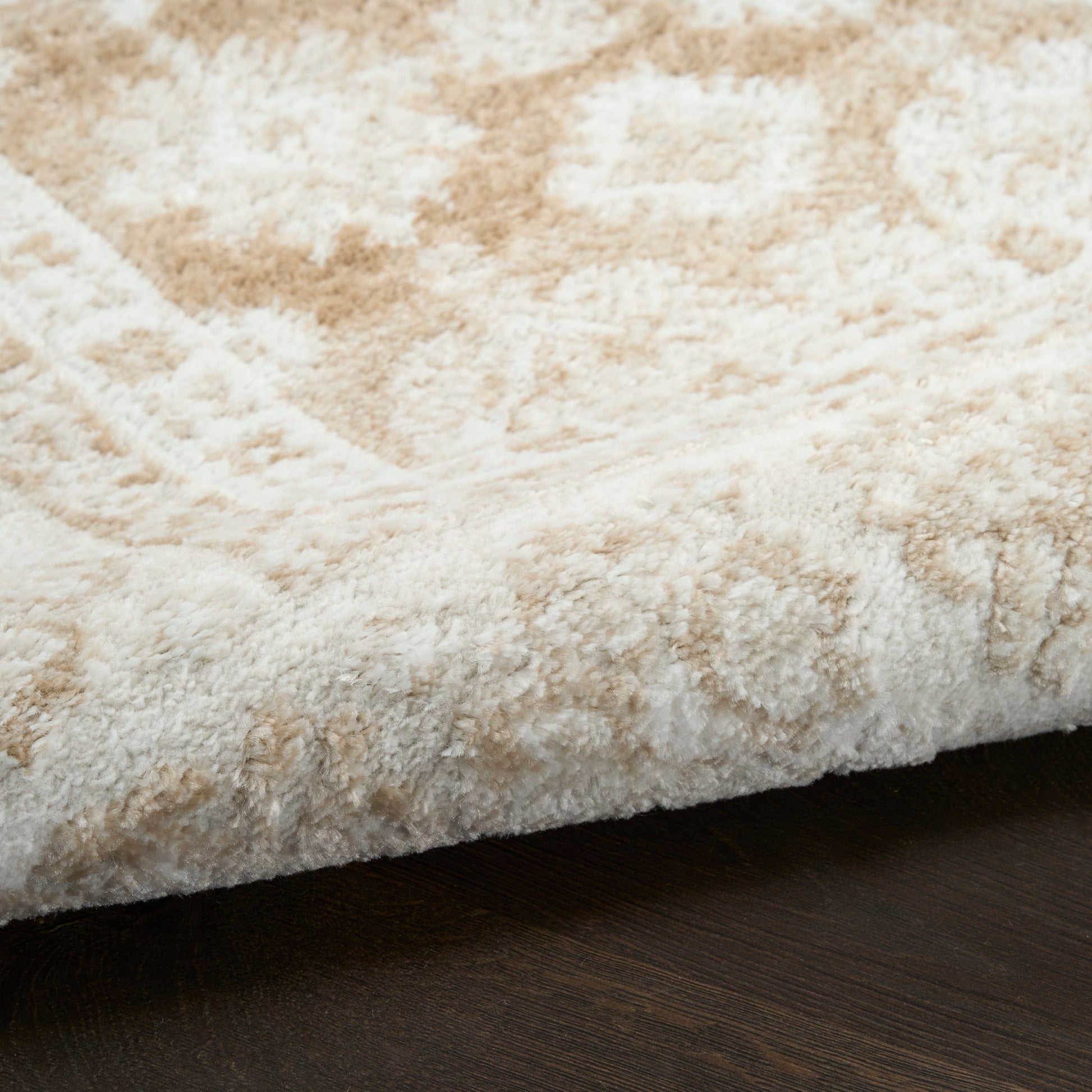 Close-up of a plush beige and cream shag rug edge resting on a dark wood floor