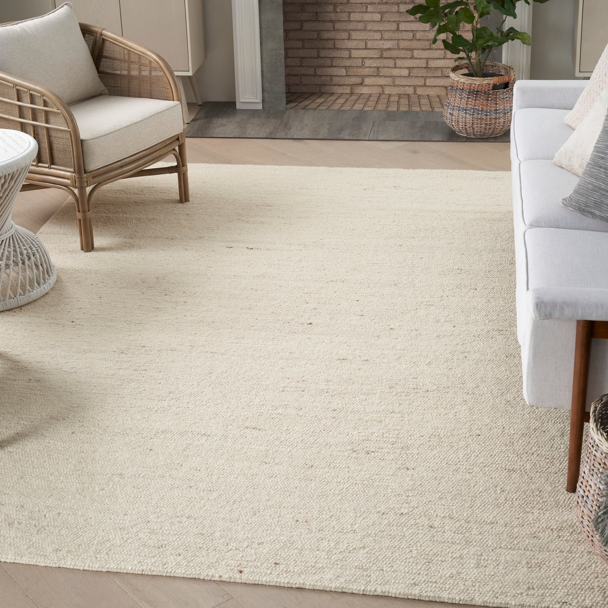 Natural beige jute rug in a farmhouse living room with a light gray sofa, wicker chair, and potted plant.