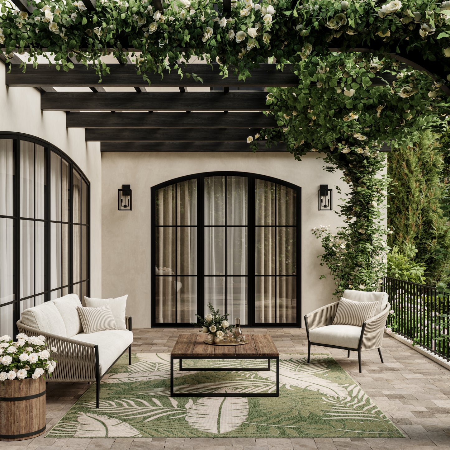 Outdoor rug with a green leaf pattern under a vine pergola, with beige cushioned seating and black metal patio furniture nearby.