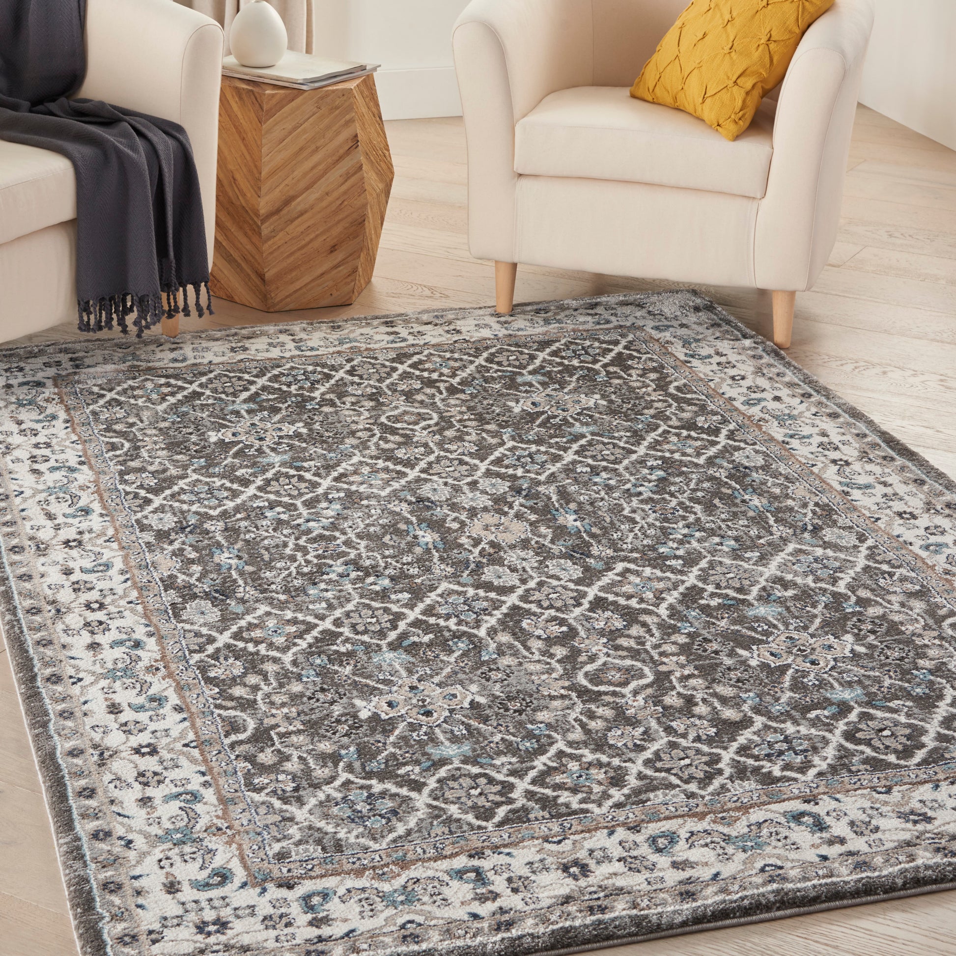 Distressed Moroccan-style area rug in gray, ivory and blue tones on a light wood floor with white chairs nearby.
