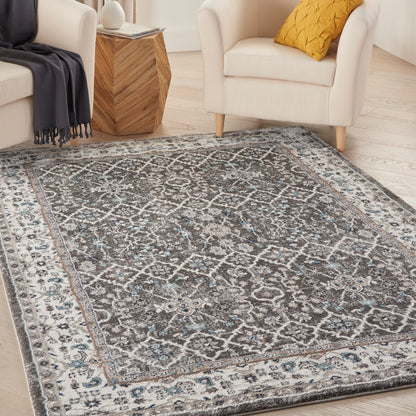 Distressed Moroccan-style area rug in gray, ivory and blue tones on a light wood floor with white chairs nearby.