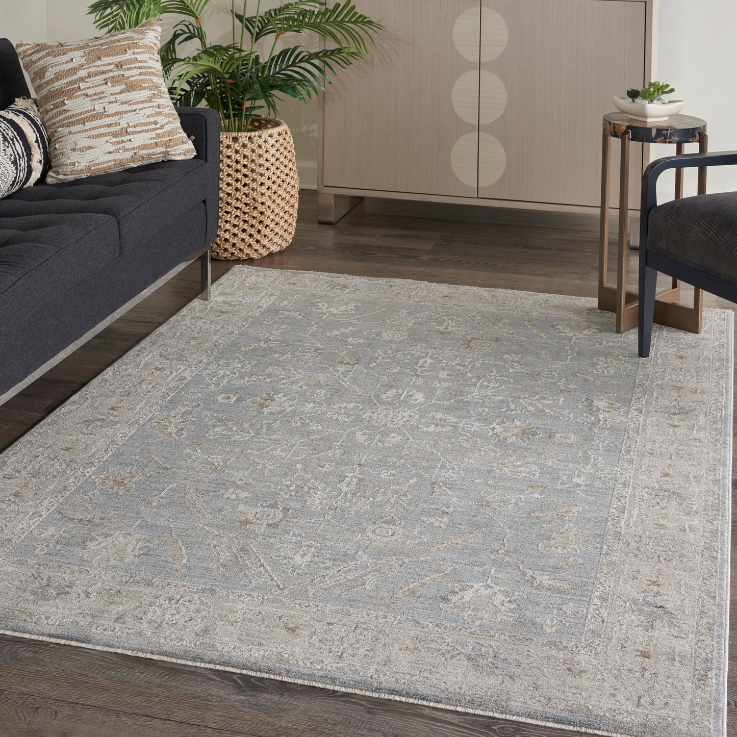 Light gray patterned area rug on dark wood floor in a modern living room with navy sofa, greenery, a woven basket, and a round side table.
